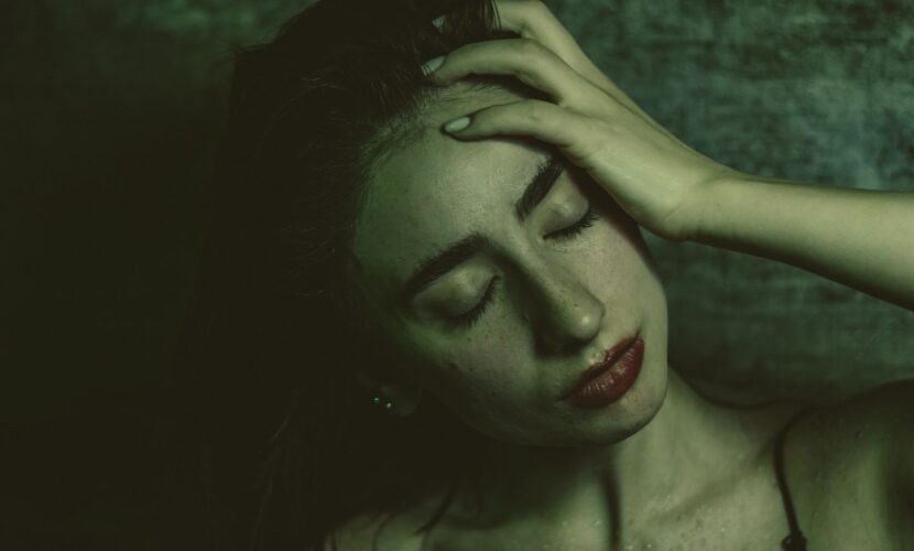 Moody portrait of a woman with closed eyes in a black tank top against a textured wall.
